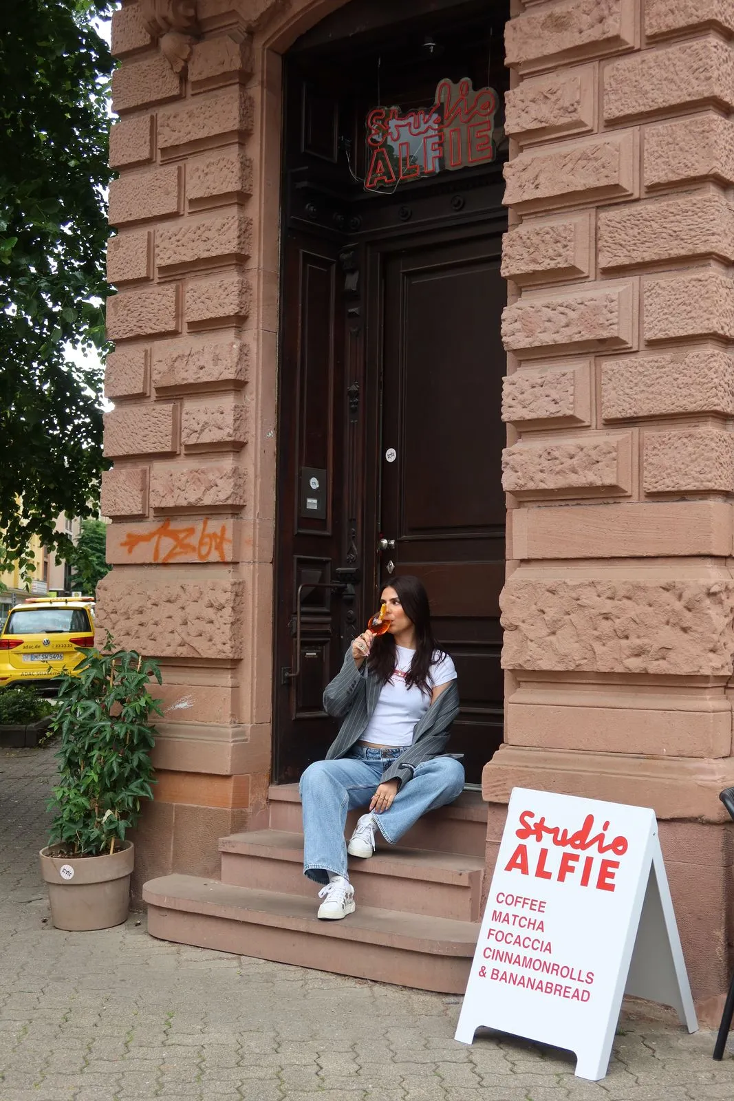 Gast mit Spritz auf den Eingangsstufen neben dem Aufsteller