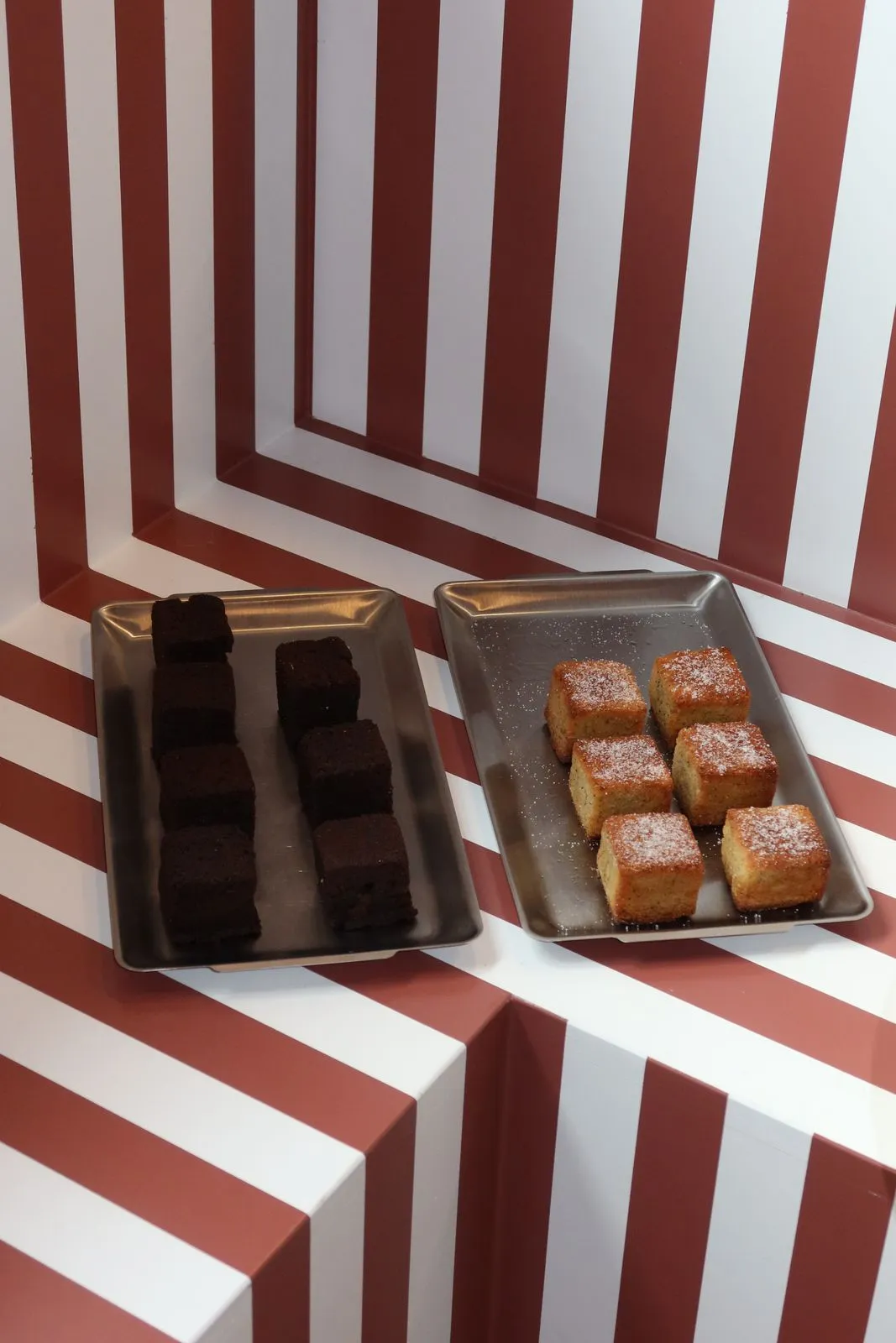 Brownies und helle Kuchenstücke auf Tabletts vor der gestreiften Wand